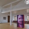 Sabile Makslas Culture and Tourism Center has a white interior with wooden chairs and artwork in the middle of the room