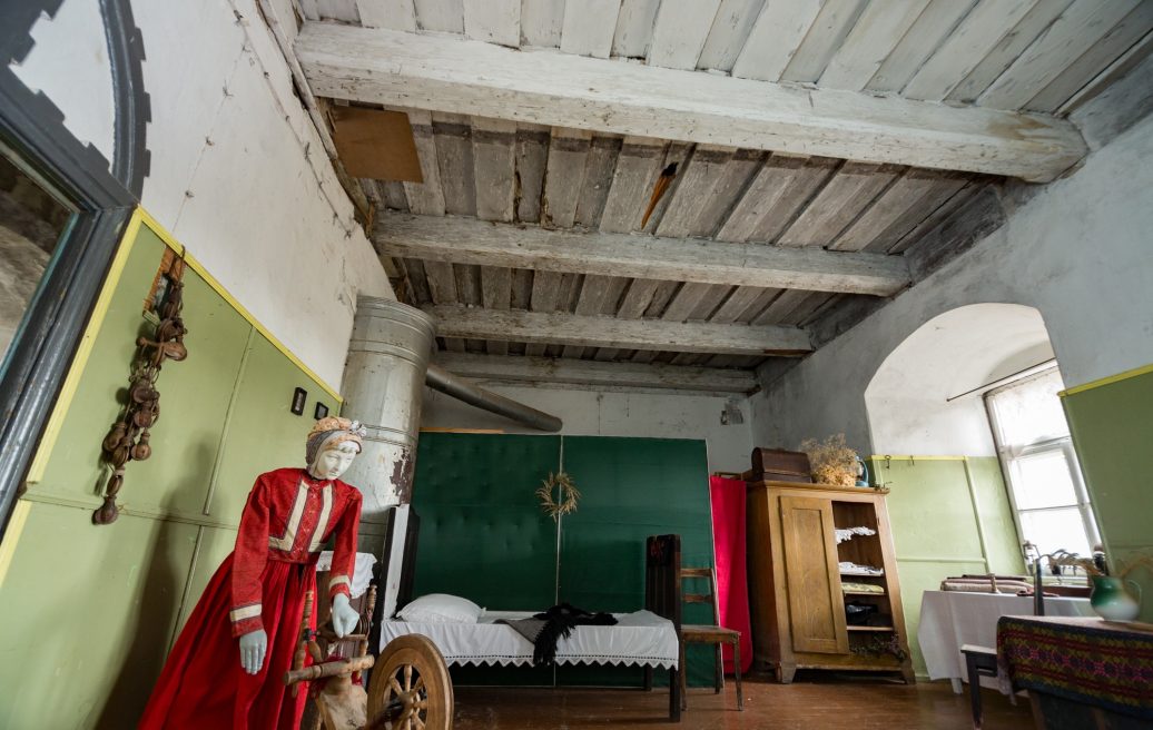 The interior of Alsunga Castle with an exhibit of medieval clothing, a bed, a chest of drawers