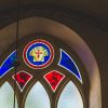 Cēsu Sv. Jāņa baznīcas loga vitrāža ar sarkaniem, ziliem un dzelteniem elementiem un krustu