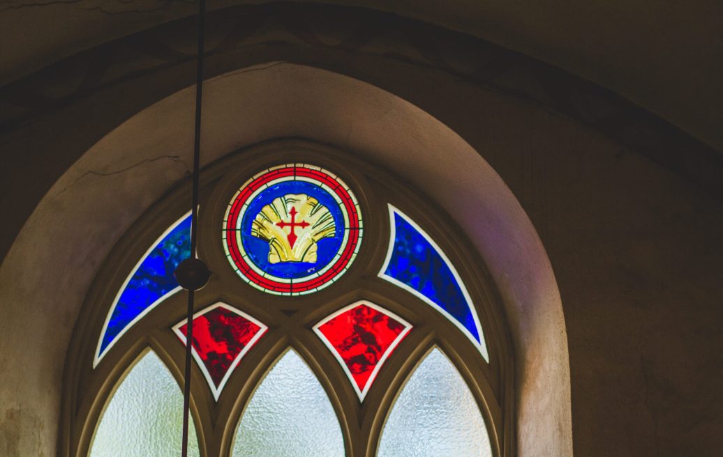Cēsu Sv. Jāņa baznīcas loga vitrāža ar sarkaniem, ziliem un dzelteniem elementiem un krustu