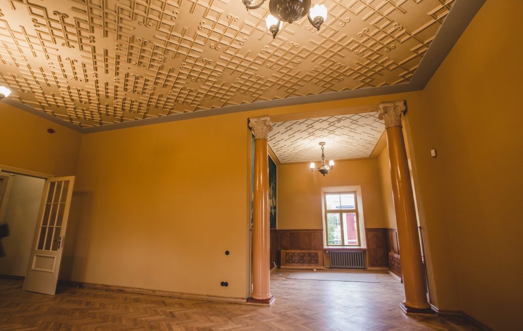 The renovated room of Sigulda's New Castle is yellow with a white ceiling and two chandeliers