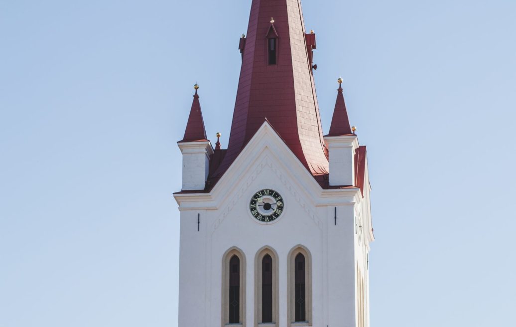 Cēsu Sv. Jāņa baznīcas torņa smaile ar krustu torņa smailes galā, baznīcas pulksteni un logiem