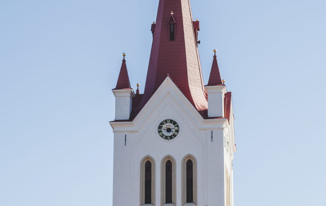 St. John’s Church in Cēsis tower with a cross at the top of the spire, church clock and windows