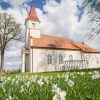 Rubenes evaņģēliski luteriskā baznīca sānskatā vasaras dienā ar ziediem priekšplānā