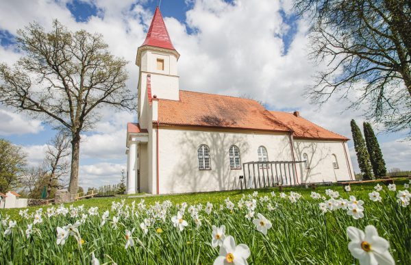 Rubenes evaņģēliski luteriskā baznīca sānskatā vasaras dienā ar ziediem priekšplānā