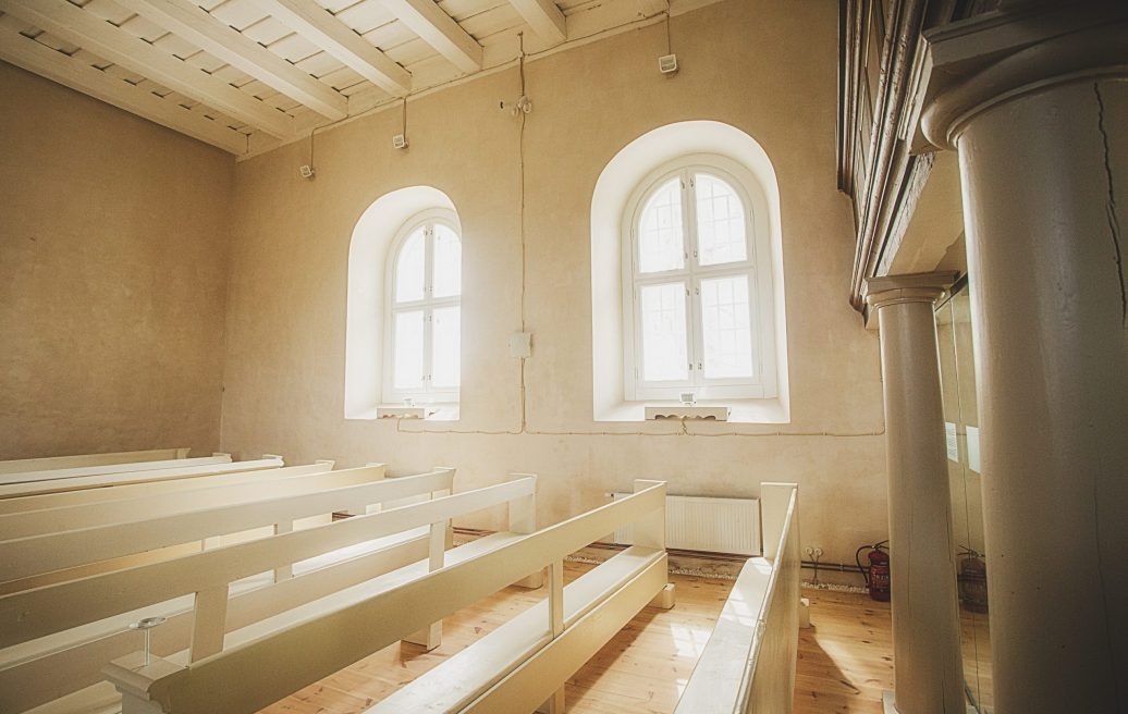 The white room of the Rubene Evangelical Lutheran Church showing windows, white seats, colonnades