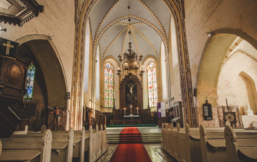 The altar of St. John's Church, where three holy candles are lit, a chandelier is visible, seats on the sides, a red carpet on the ground