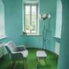 Krustpils Palace lounge with blue walls and a green carpet floor. In the room there is a gray chair with a footrest.