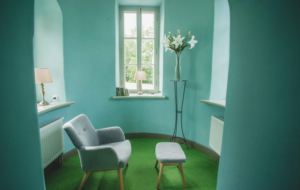 Krustpils Palace lounge with blue walls and a green carpet floor. In the room there is a gray chair with a footrest.
