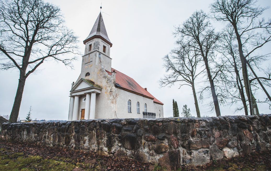 Rubenes evaņģēliski luteriskā baznīca ar mūri un kokiem apkārt
