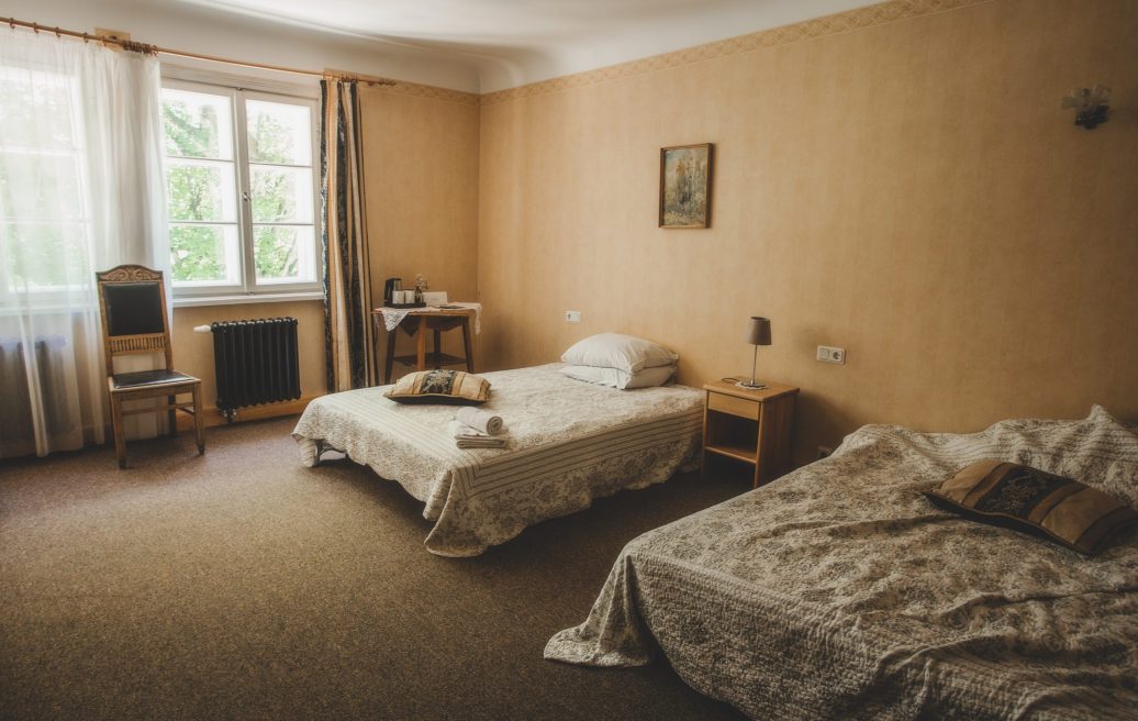 Ungurmuiža bedroom with two beds, chair, window, lamp, table and white curtains