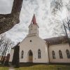 Smiltenes evaņģēliski luteriskā baznīca ainavā ar kokiem un sauli un mākoņainām debesīm