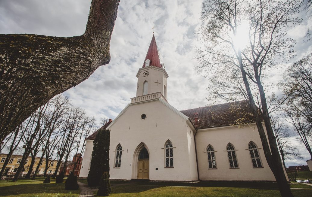 Smiltene Evangelical Lutheran Church in a landscape with trees and sun and cloudy sky